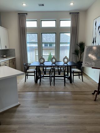 Model Home A modern dining area with large windows, a sleek black table, elegant chairs, and wooden flooring.