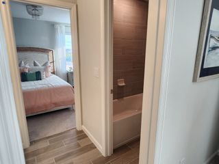 A cozy bedroom with soft peach bedding and a wicker headboard, adjacent to a modern bathroom with tiled walls.