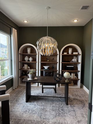 A sophisticated home office with built-in shelves, modern chandelier, and large window.