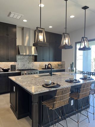 A chic kitchen with dark cabinets, marble countertops, and stylish pendant lighting over a central island with wicker chairs.