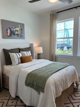 Cozy bedroom featuring a plush bed with mixed pillows, a green throw, modern lamp, and chic tractor artwork.