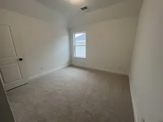 A cozy, carpeted room with a neutral palette and abundant natural light from a single window.