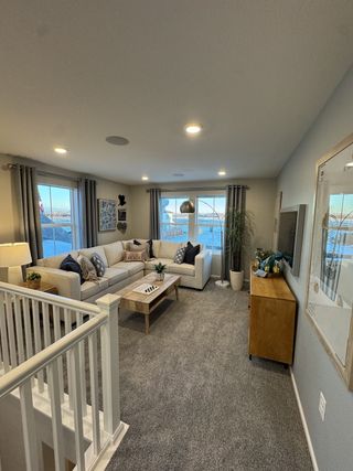 Model Home A cozy living room with a plush L-shaped sofa, soft grey carpet, and modern decor, featuring large windows with serene views.