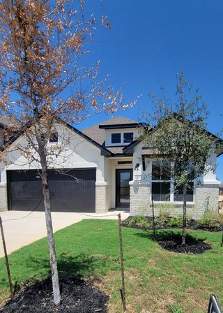 A charming single-story home with a stone and stucco facade, featuring a dark garage door and landscaped yard, in Davis Ranch by Coventry Homes (San Antonio, TX). 