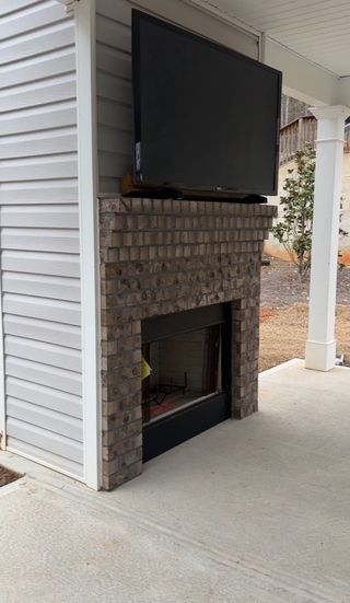 A charming outdoor brick fireplace with a mounted TV on a covered patio in Covington by Castle Homes (Savoy Park, GA).