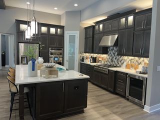 A modern kitchen featuring dark wood cabinets, stainless appliances, a spacious island, and sleek pendant lighting.