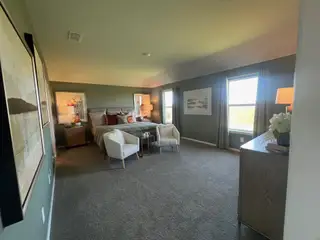 Model Home A spacious bedroom with cozy seating, elegant decor, and warm natural light from large windows.