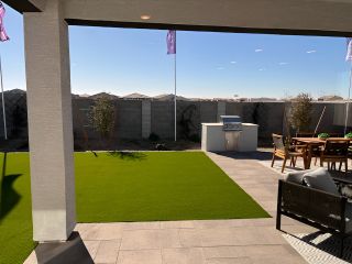 A modern backyard with synthetic lawn, patio, barbecue grill, and seating area perfect for outdoor gatherings.