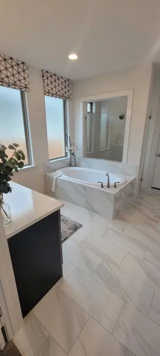A relaxing bathroom retreat with a soaking tub, marble-look tile, and large frosted windows, creating a serene and bright atmosphere.