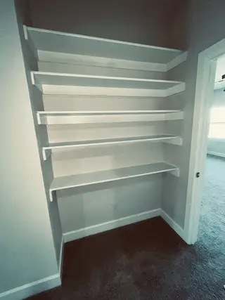 Built-in white shelving unit within a cozy carpeted nook, perfect for organizing books or displaying decor items.