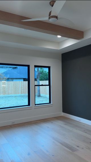 Model Home Bedroom: A spacious bedroom featuring large windows, a dark accent wall, and a tray ceiling with a sleek ceiling fan.
