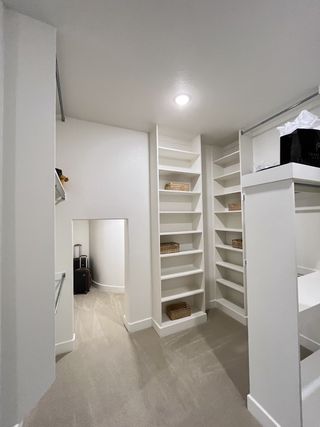 Model Home A spacious walk-in closet with built-in shelves and soft carpeting, offering ample storage and organization options.