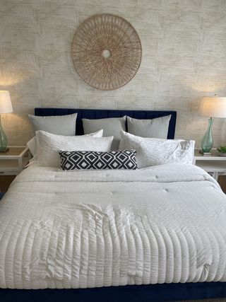 A cozy bedroom with a textured accent wall, plush white bedding, striped pillows, and elegant bedside lamps.