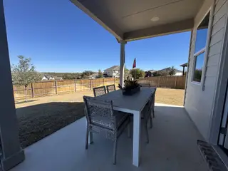Model Home A cozy patio with a modern dining set overlooks a spacious fenced backyard and clear blue sky.