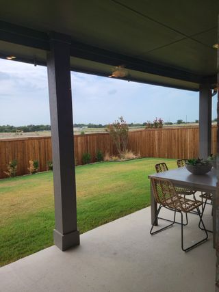 Model Home A cozy backyard patio with a modern dining set, overlooking a green lawn and wooden fence.