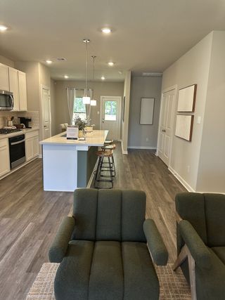 An inviting kitchen with wood floors, modern island, green chairs, and elegant pendant lighting.