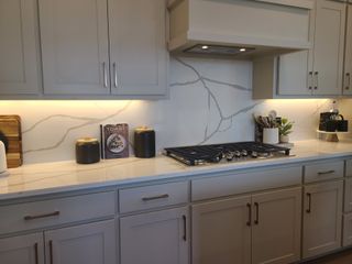 A modern kitchen with sleek cabinetry, marble-patterned backsplash, and ambient under-cabinet lighting.