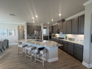A modern kitchen with gray cabinetry, stainless steel appliances, a granite-topped island with plush bar stools, and wood-look tile flooring.