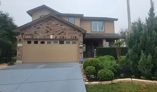A two-story home in Laurel Vistas by D.R. Horton (San Antonio, TX) features a mix of brick and siding, a two-car garage, and mature landscaping.