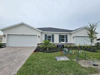Street view A beautiful white home with a dual garage, stone accents, and lush landscaping in Hammock Oaks Villas by Ryan Homes (Lady Lake, FL).