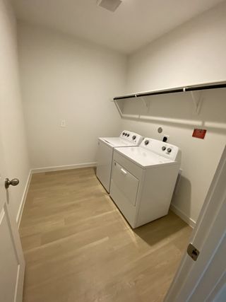 A functional laundry room with natural wood flooring, equipped with modern washer and dryer, and overhead shelving.