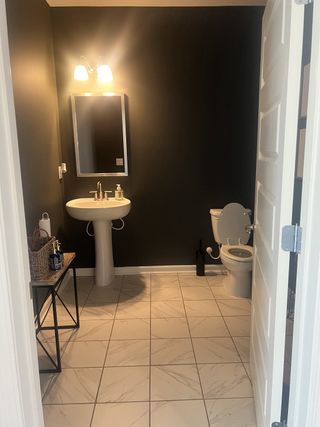 Model Home A sleek bathroom with dark walls, a pedestal sink, and a tiled floor. Modern lighting adds elegance.