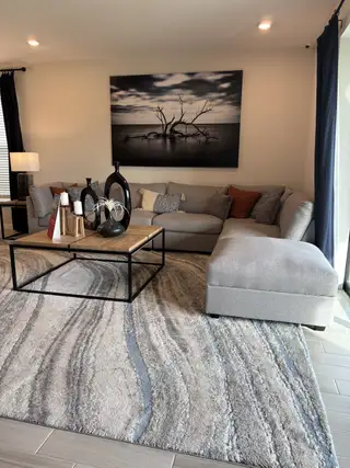 Model Home A cozy living room featuring a plush sectional sofa, abstract artwork, and a modern rug for an inviting ambiance.
