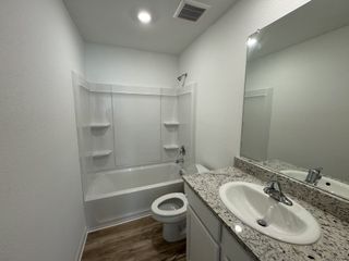 A sleek bathroom featuring a granite countertop, wooden floors, and a pristine bathtub with integrated shelving.