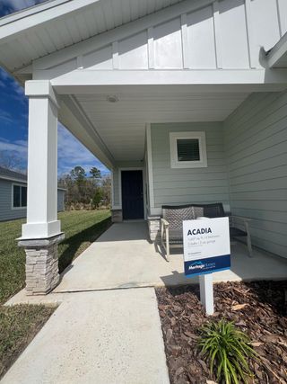A welcoming covered porch in Kings Preserve (Jacksonville, FL) by Meritage Homes features a light gray exterior, stone accents, and an "Acadia" model sign.