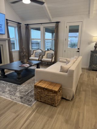 A cozy living room with a light wood floor, plush sofa, dark coffee table, and elegant armchairs by large windows.