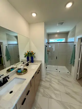A modern bathroom with dual sinks, marble-patterned floor tiles, a glass shower, and elegant fixtures.