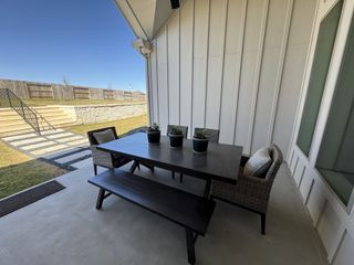 A cozy patio with a sleek dark table, wicker chairs, and potted plants, perfect for outdoor relaxation.