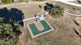 A spacious community basketball court surrounded by greenery in Brooks Ranch by D.R. Horton (Kyle, TX).