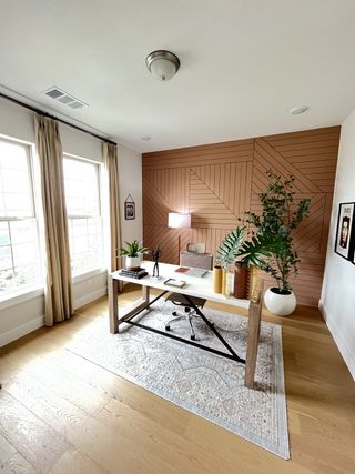 A chic home office featuring a wooden accent wall, large windows, and stylish decor with a modern desk and seating.
