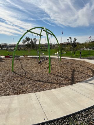 Community Amenities A vibrant playground with modern swings and lush greenery in IronWing at Windrose by Brightland Homes (Litchfield Park, AZ).
