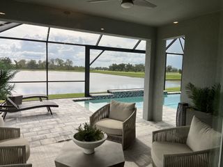 A serene patio with plush seating, overlooking a tranquil pool and scenic waterfront view, surrounded by lush greenery.