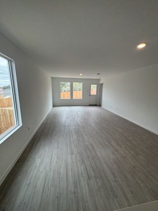 A spacious living room with light wood flooring, large windows, and crisp white walls, inviting natural light.