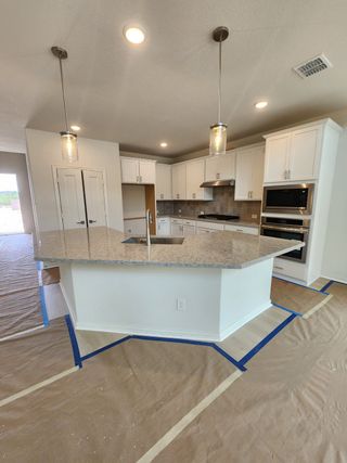 Model Home A modern kitchen featuring a large granite island, white cabinetry, stainless steel appliances, and elegant pendant lighting.