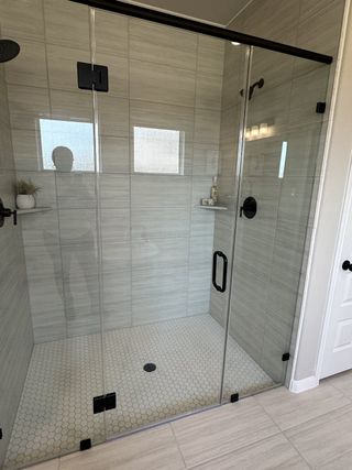A sleek shower with glass doors, textured tile walls, and hexagonal floor tiles. Modern fixtures and subtle decor add elegance.
