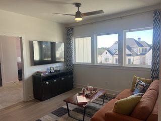A cozy living area with large windows, an orange sofa, patterned curtains, and a wall-mounted TV, bathed in natural light.