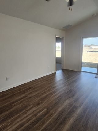 A bright room with elegant wood flooring and large windows opening to a yard view, inviting natural light and warmth.