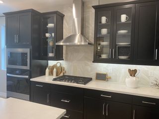 A modern kitchen boasts dark cabinetry, stainless steel appliances, and a sleek range hood, blending style and functionality with clean lines.
