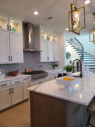 Model Home A modern kitchen with white cabinetry, elegant pendant lights, and a sleek spiral staircase in the background.