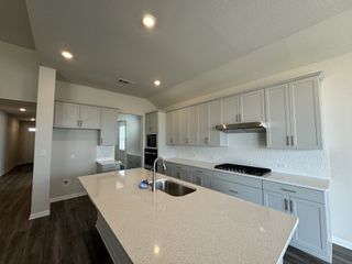 A modern kitchen with gray cabinets, a large island, quartz countertops, and sleek stainless steel appliances.
