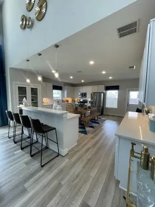 Model Home A modern kitchen with sleek white cabinets, a large island, pendant lights, and stylish wood flooring.