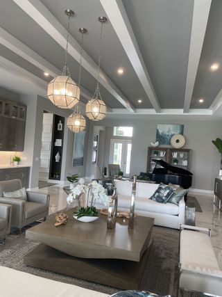 Elegant living room with modern lighting, coffered ceiling, plush seating, and a grand piano centerpiece.