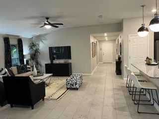 A modern living area with sleek tile flooring, black accents, a cozy sectional, and a stylish open kitchen with bar seating.