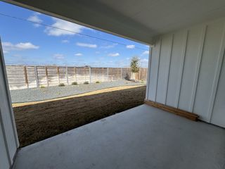 Model Home A covered patio with a view of a spacious backyard featuring a gravel area and privacy fence.