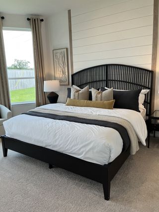 A cozy bedroom featuring a stylish black bedframe, elegant pillows, and a shiplap accent wall with warm natural light.