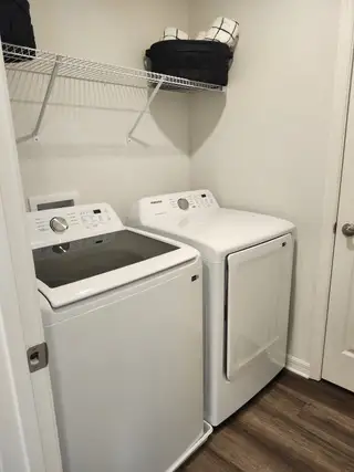 A compact laundry room featuring modern appliances, open shelving, and wood-like flooring.